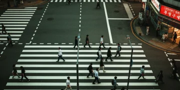An aerial, high-contrast photograph of a diverse crowd of people moving across a busy city intersection at dusk, symbolizing global power shifts.